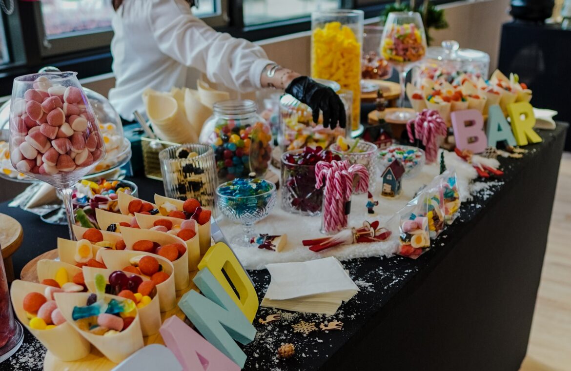 candy-station-christmas-buffet-host-holiday-event-catering-miami Candy station with host handing out sweets at Taste Corner’s scenographic Christmas buffet during a festive event in South Florida